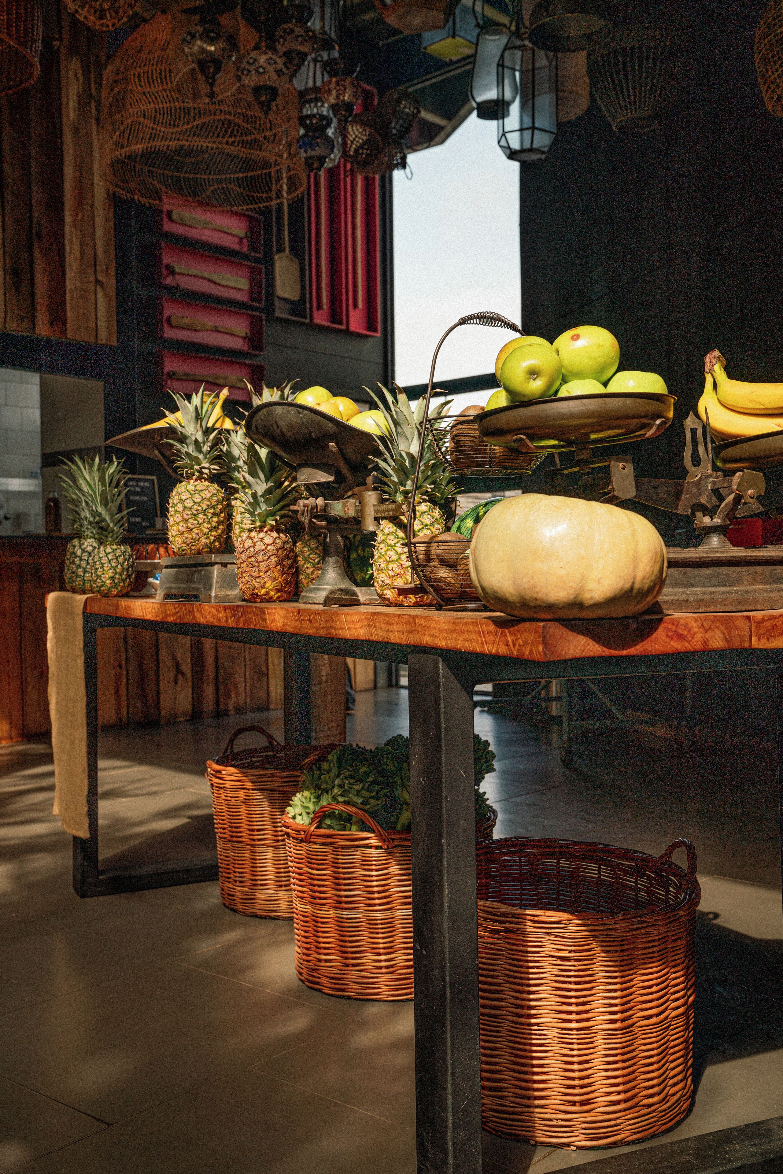 Une table en bois avec des fruits, une grosse citrouille et des paniers en osier.