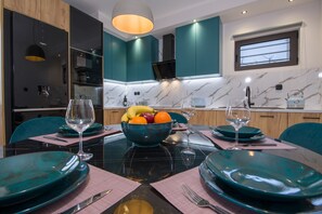 A modern kitchen with teal cabinets, a marble countertop, and a dining area set with teal plates and glasses. - Anastasia & Marie luxury & traditional residence with large jacuzzi 1 minute sea (Κίσσαμος)