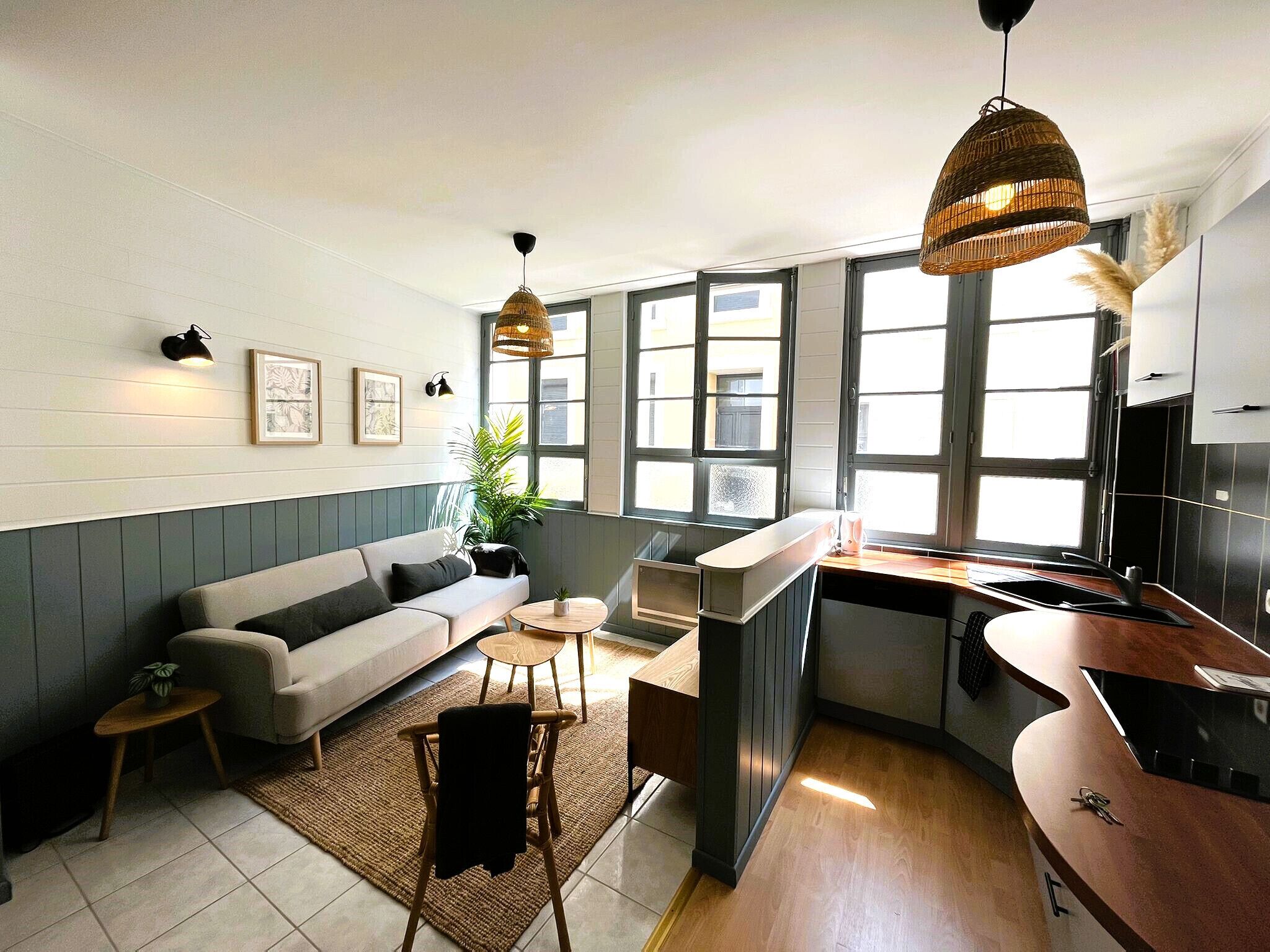 Una cocina moderna con estufa integrada, zona de comedor con sofá y una mesa pequeña, y ventanas amplias que dejan entrar luz natural.