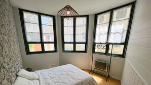 Un dormitorio con cama, radiador y ventana con vistas a edificios.