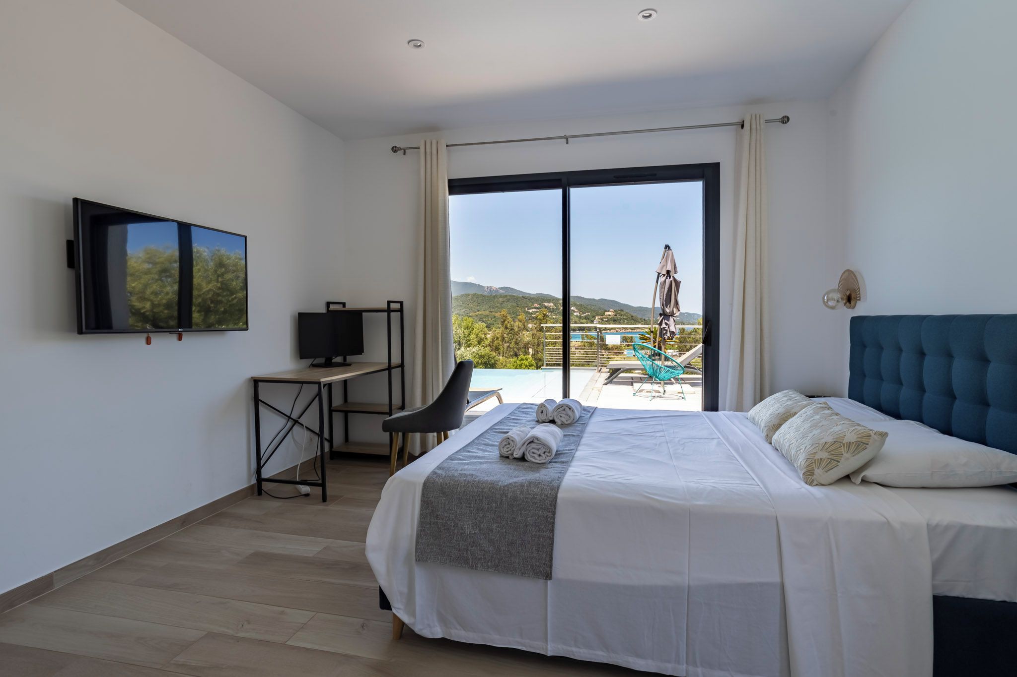Ein Hotelzimmer mit Bett, Schreibtisch mit Fernseher und Blick auf Pool und Berge.