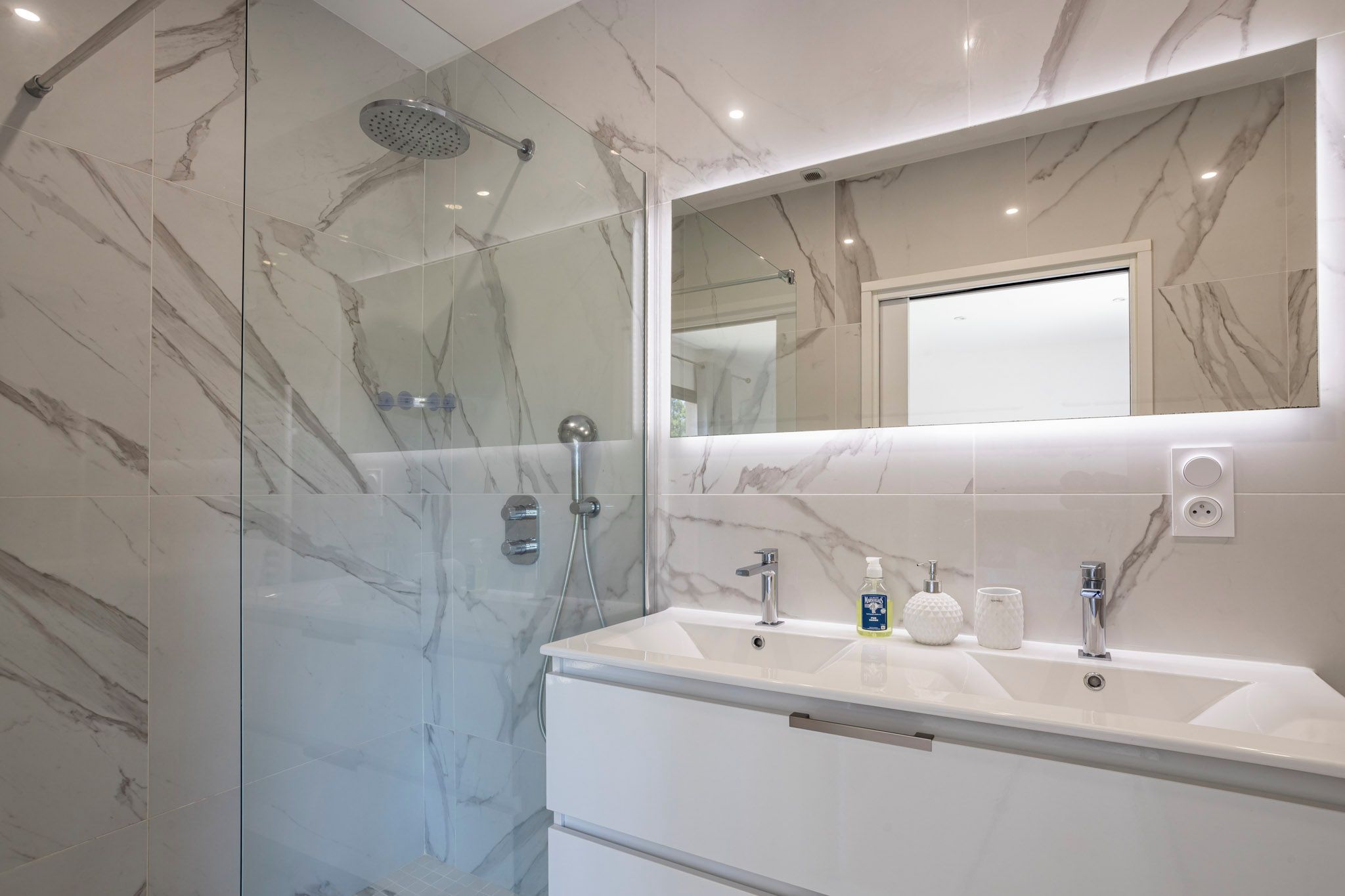 Un bagno moderno con doccia vetrata, un ampio specchio e un mobile vanità bianco con due lavabi.