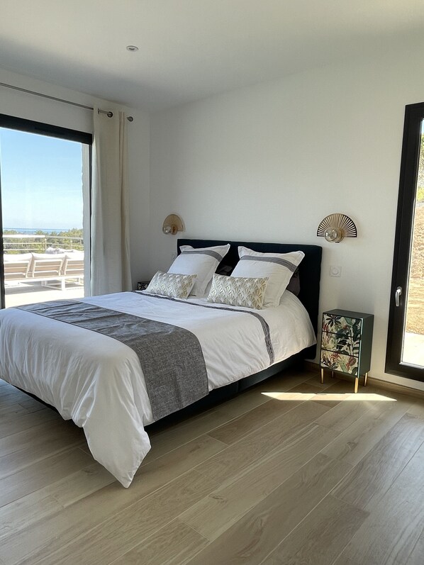 A modern bedroom with a large bed, a nightstand, and a view of the outdoors. - New villa with large heated pool and sea view (Conca)
