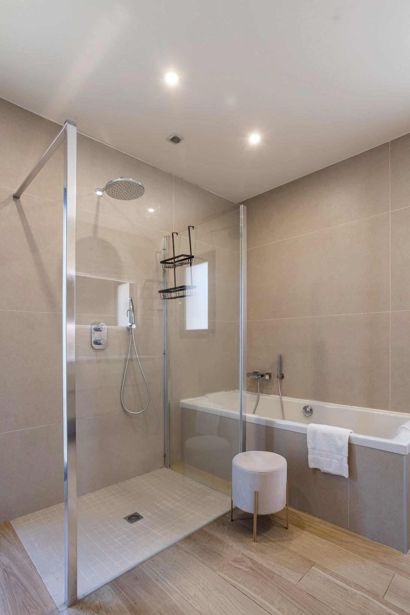 A modern bathroom with a glass-enclosed shower, a freestanding bathtub, and a small stool.