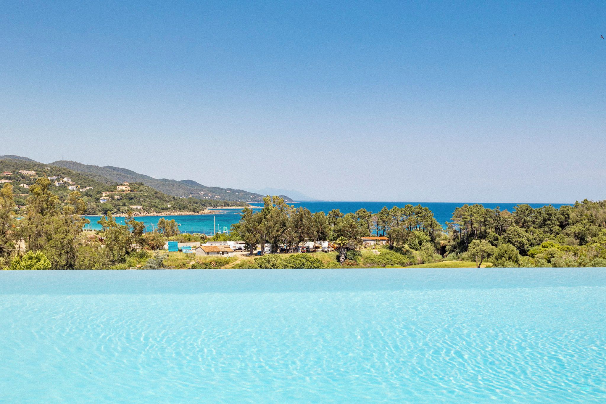 A clear blue pool with a view of a coastal area, including a beach and buildings in the distance.