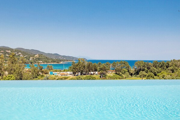 A clear blue pool with a view of a coastal area, including a beach and buildings in the distance.