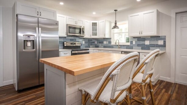 A modern kitchen with white cabinets, a stainless steel refrigerator, a microwave, and a wooden island with two wicker chairs. - Modern Farmhouse Retreat – Heated Pool & Close to Beaches! (Stuart)