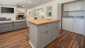 A modern kitchen with grey cabinets, a wooden countertop, and a built-in washing machine. - Modern Farmhouse Retreat – Heated Pool & Close to Beaches! (Stuart)