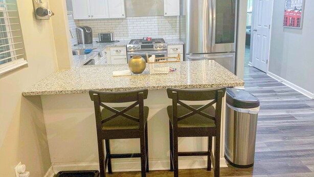 A kitchen with a granite countertop, stainless steel appliances, and two wooden chairs.