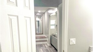 A hallway with a light-colored floor, a door on the left, and a light switch on the right.