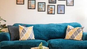 A teal sofa with patterned cushions, a wooden side table with a book and a plant, and a wall with framed artwork. - Stay in this cozy and bright 2BR apartment, featuring a welcoming living room, modern décor, and plenty of natural light. Walk to Calle Ocho cafés, murals, and music, and reach Brickell in minutes. Perfect for families or groups exploring Miami (Miami)