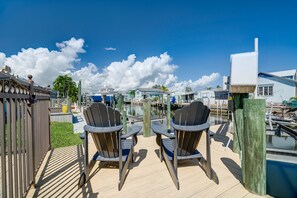 A deck with two Adirondack chairs facing a marina with boats and a house in the background.