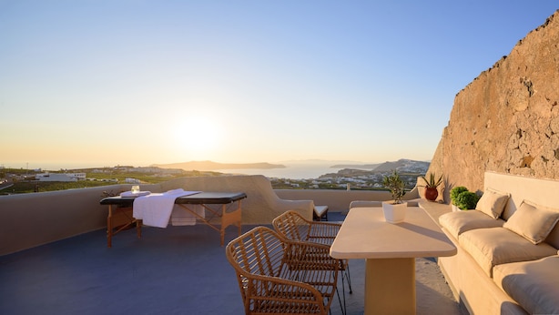 Eine Terrasse mit Tisch, Stühlen und einer Couch, mit Blick auf eine reizvolle Landschaft mit Bergen und einem Gewässer.