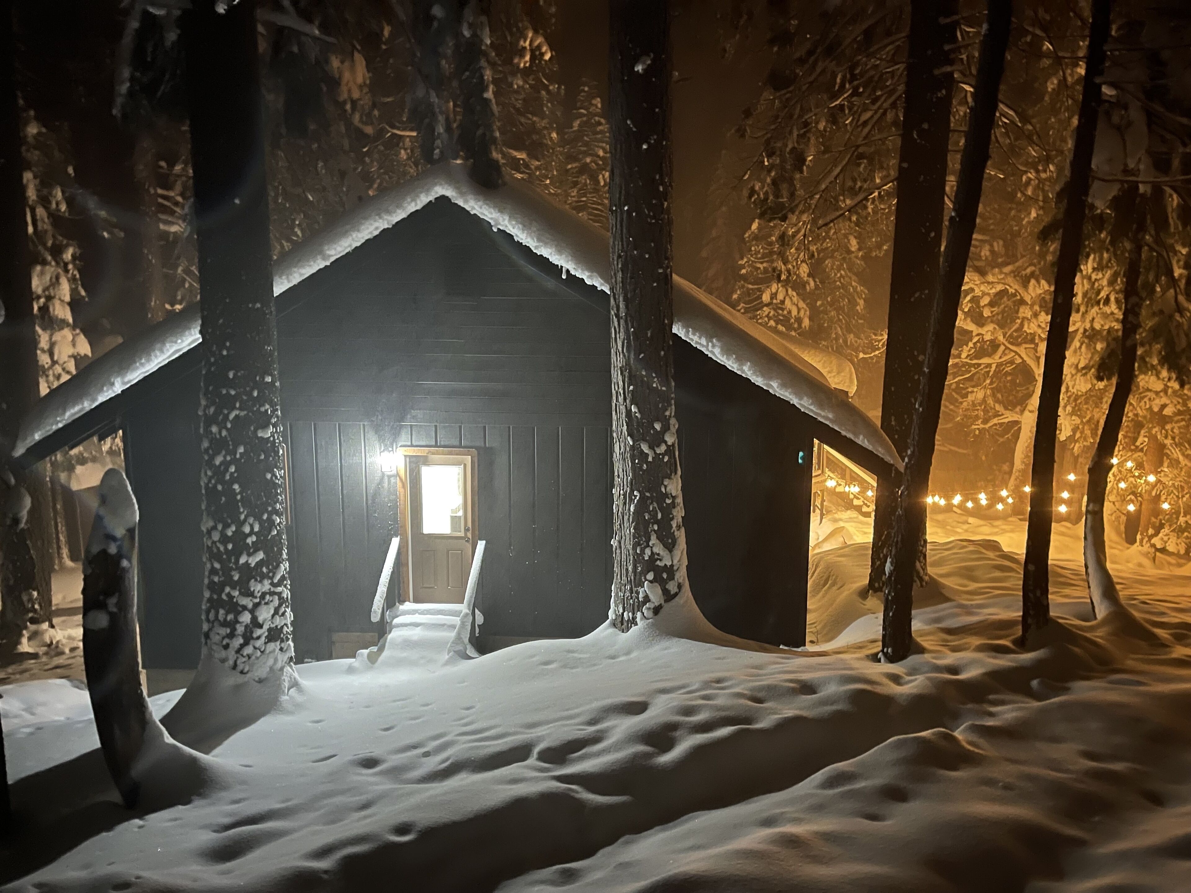 A snow-covered cabin with a wooden door and a visible interior light.
