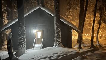 A snow-covered cabin with a wooden door and a visible interior light.
