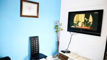 Une pièce avec un mur bleu, un tableau encadré, une chaise noire, une console blanche et un téléviseur fixé au mur.