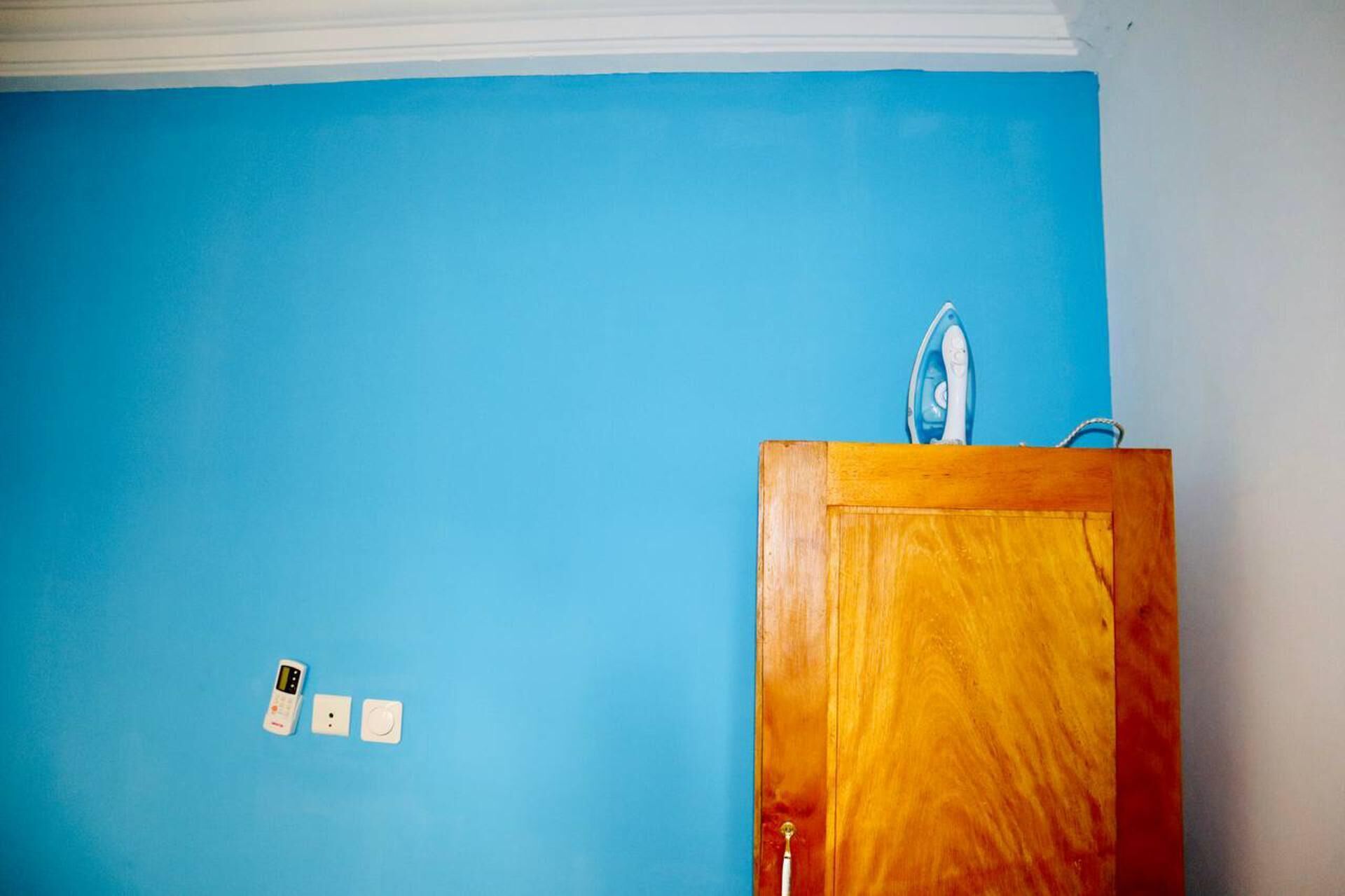 A room with a blue wall, a wooden cabinet, and a white electrical outlet with a plug.
