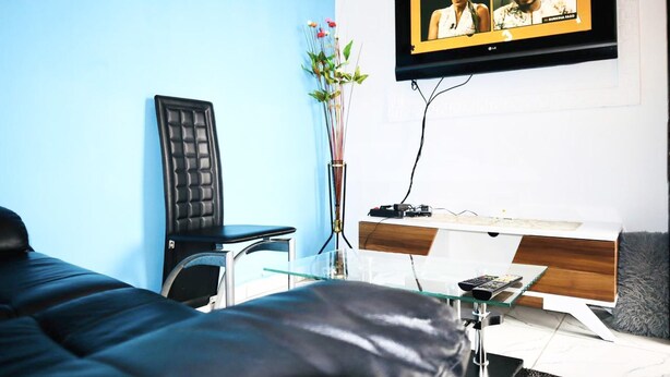 A modern hotel room with a bed, a desk with a computer, a TV mounted on the wall, and a vase with flowers. - 1 Bed Studio Sleeps 2 - Canal Views, Balcony, Wifi (Douala)