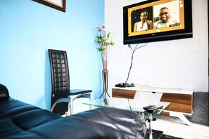 Una habitación de hotel moderna con una cama, un escritorio con computadora, un televisor montado en la pared y un florero con flores.