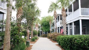 A pathway flanked by palm trees and a hedge, leading to a building with a balcony and an American flag.