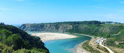 Un paisaje costero con playa, acantilados y una carretera que lleva a un área de estacionamiento.