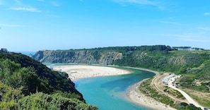 A coastal landscape with a beach, cliffs, and a road leading to a parking area.