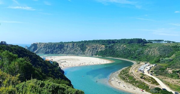 A coastal landscape with a beach, cliffs, and a road leading to a parking area.