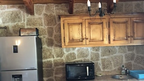 A compact kitchen with a stone wall, wooden cabinets, a stainless steel refrigerator, a microwave, and a sink. - Caseddu in the shade of the Olive Trees, just a few steps from the sea. (Olmeto)