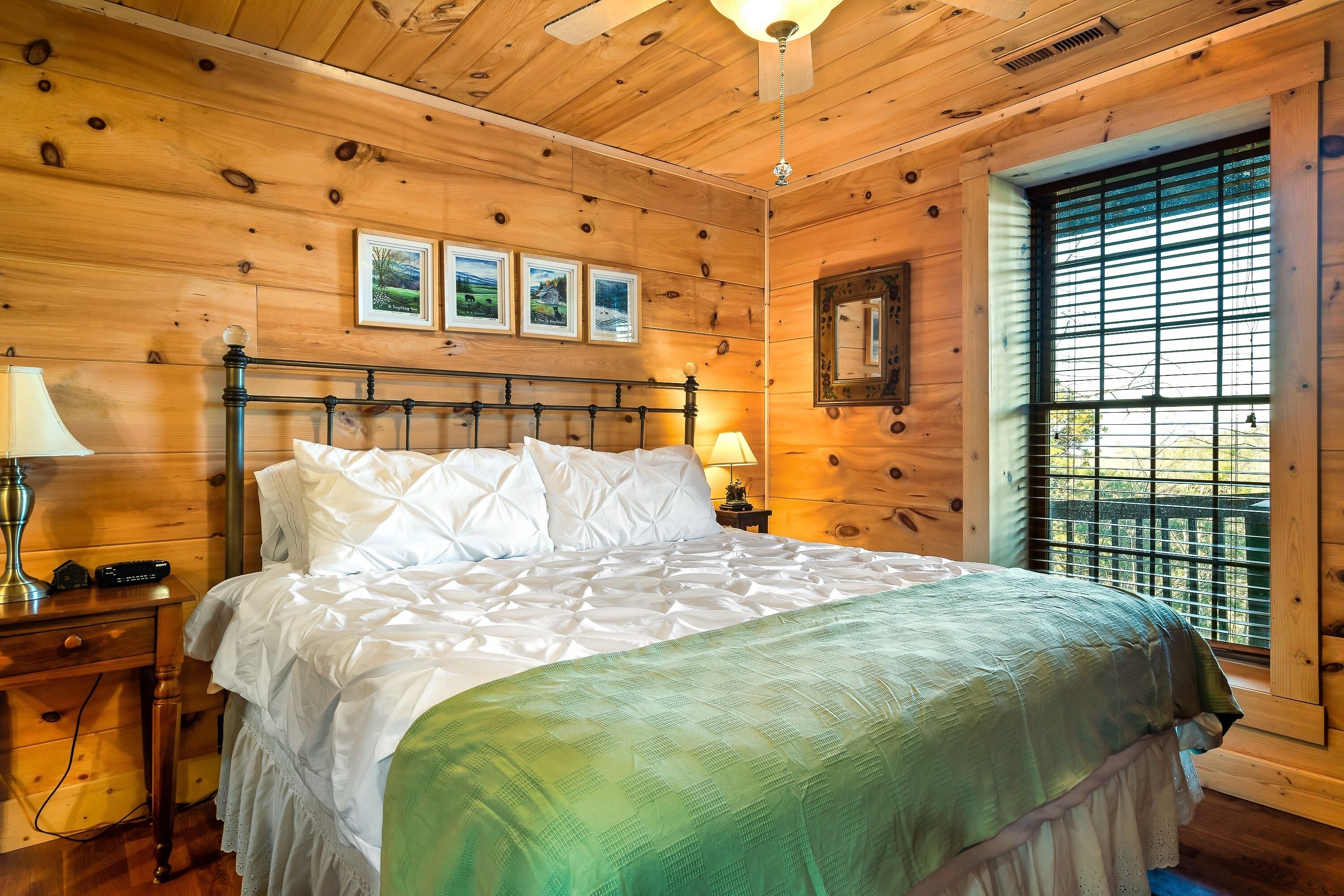 Un dormitorio con paneles de madera, una cama, lámparas de noche e imágenes enmarcadas en la pared.