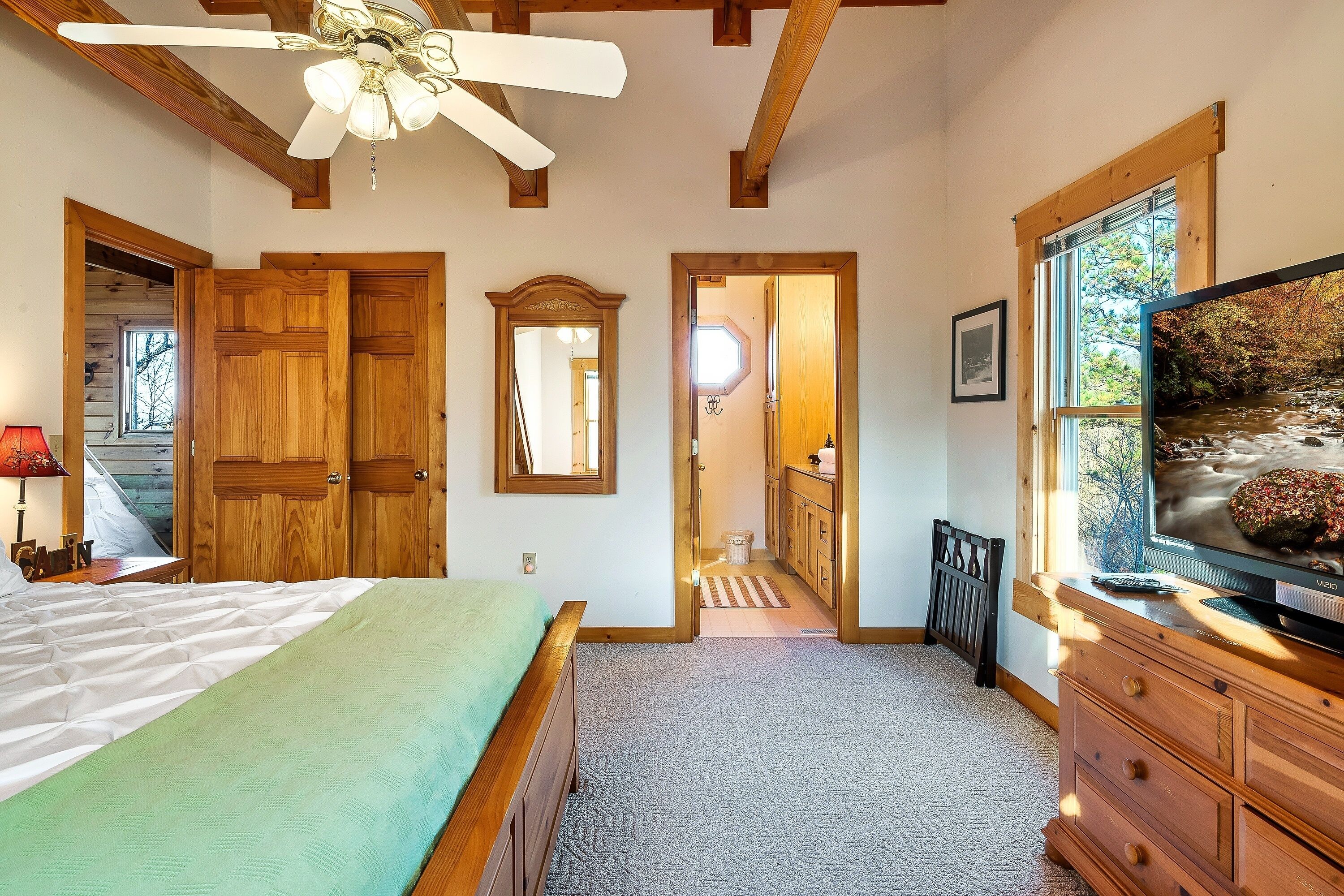 A bedroom with a bed, wooden wardrobe, a television, and a ceiling fan.