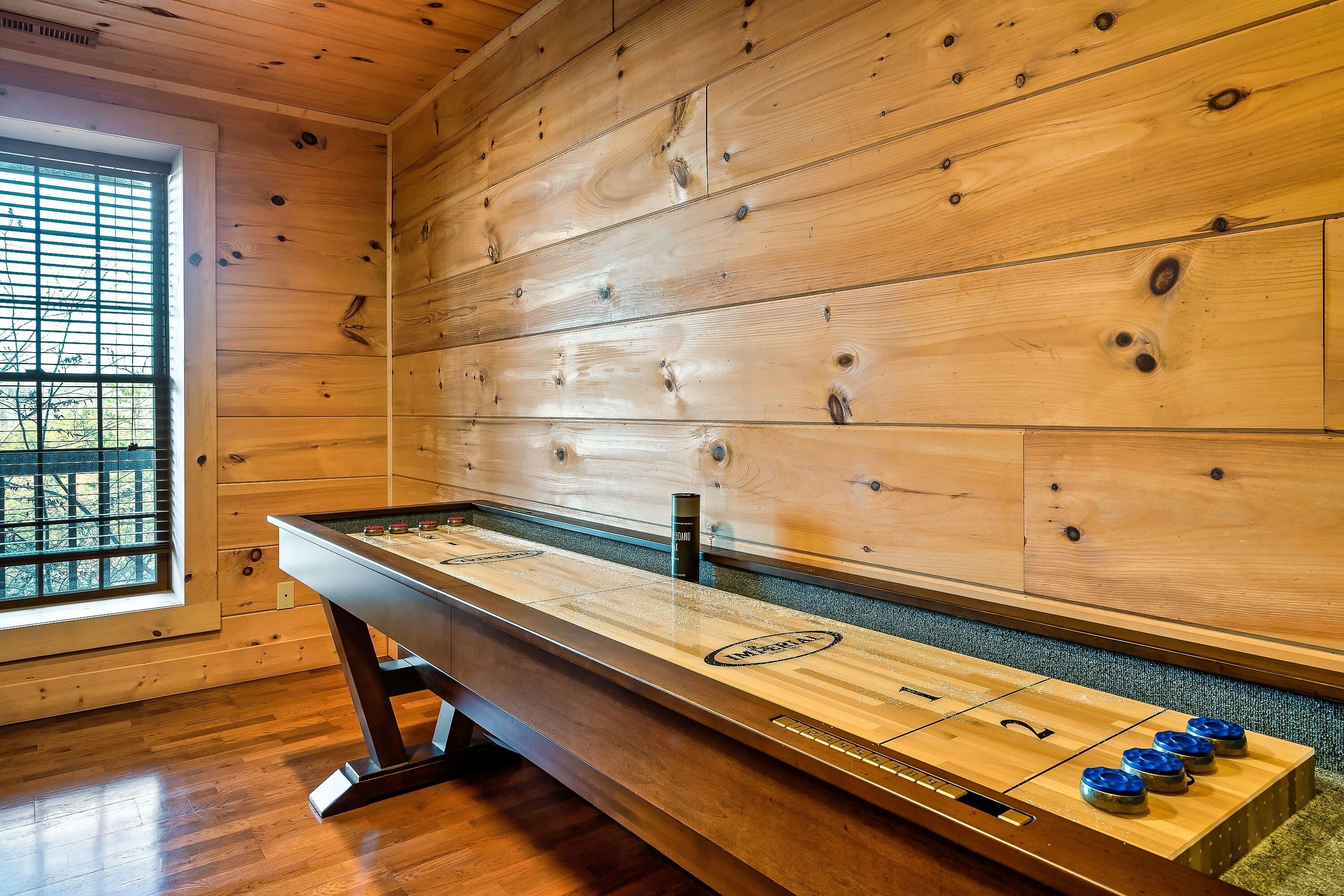 Una mesa de shuffleboard en una habitación con paredes de madera y una ventana.