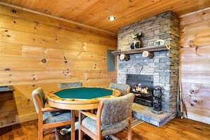 A wooden interior with a poker table, chairs, a stone fireplace, and a bear statue.