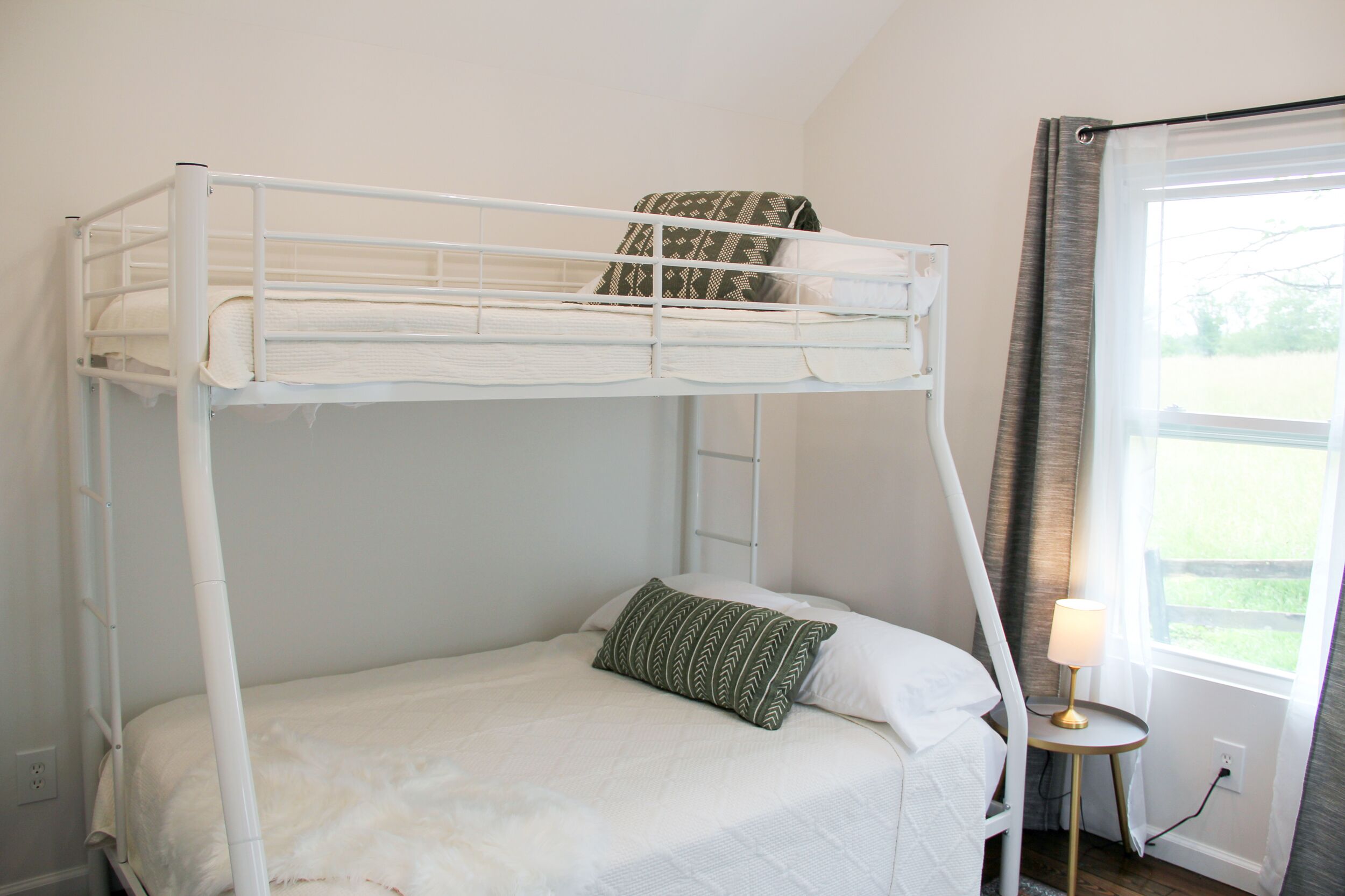 Een stapelbed met een kussen, een nachtkastje met een lamp en een raam met gordijnen.