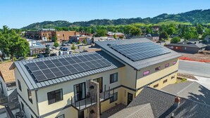 A modern two-story building with solar panels on the roof, a stone pillar, and a clear view of the surrounding neighborhood. - Downtown Executive Apartment - Pyrite (Spearfish)