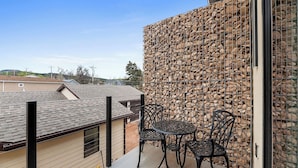 A balcony with a stone wall, two chairs, and a table. - Downtown Executive Apartment - Pyrite (Spearfish)