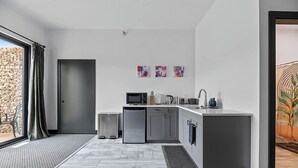 A modern kitchen with a microwave, sink, and small refrigerator. There are three artworks on the wall and a window with curtains. - Downtown Executive Apartment - Pyrite (Spearfish)