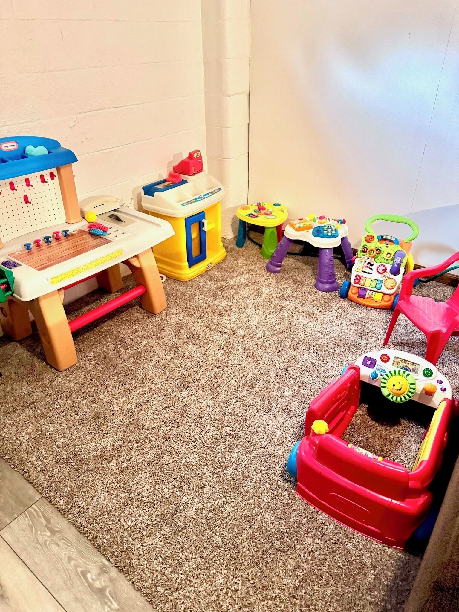 Un área de juegos con diversos juguetes y estructuras recreativas, que incluye una pequeña mesa, una cocina de juguete y un coche de juguete.