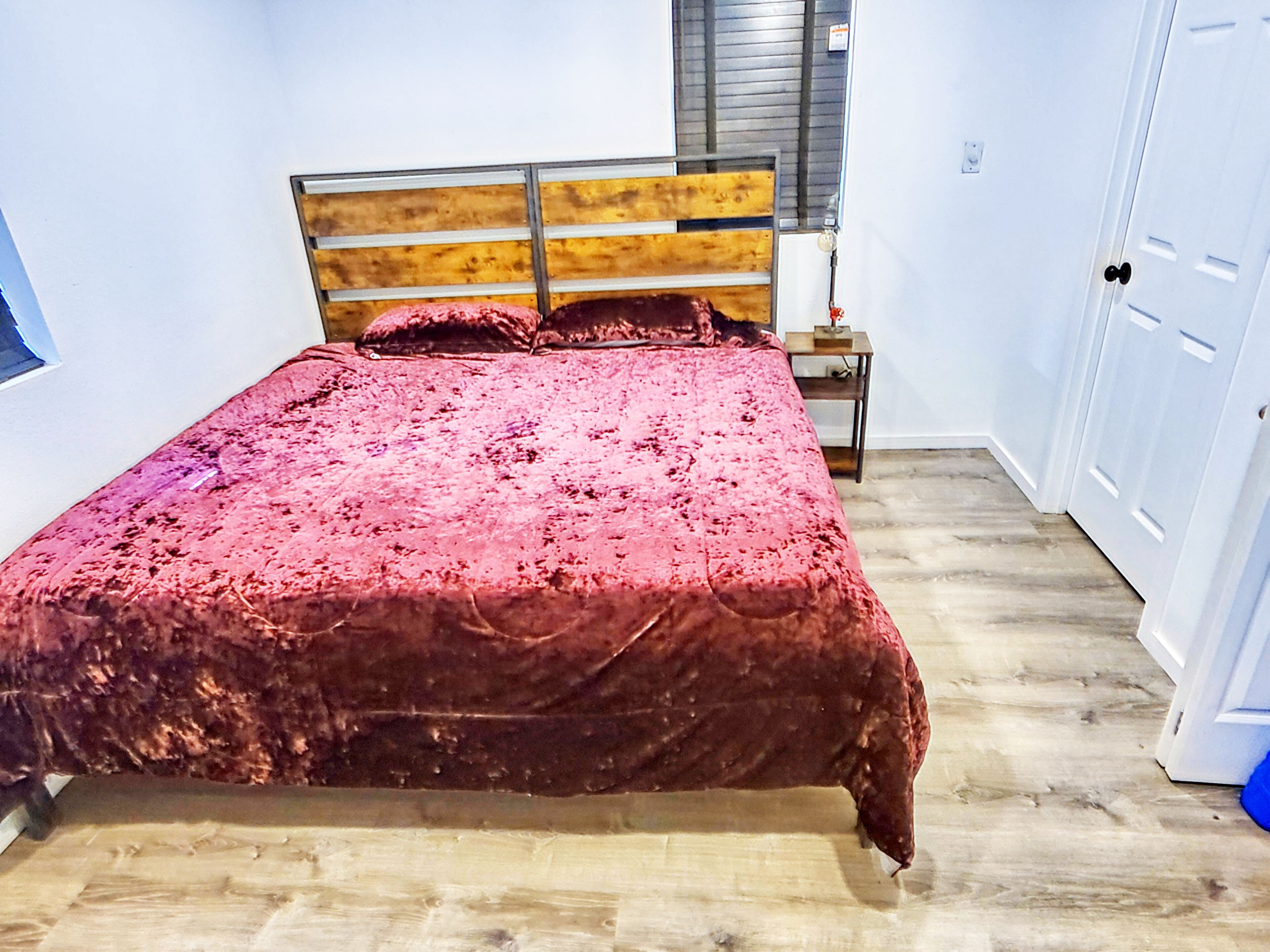 A bed with a wooden headboard, a red bedspread, and a wooden floor.