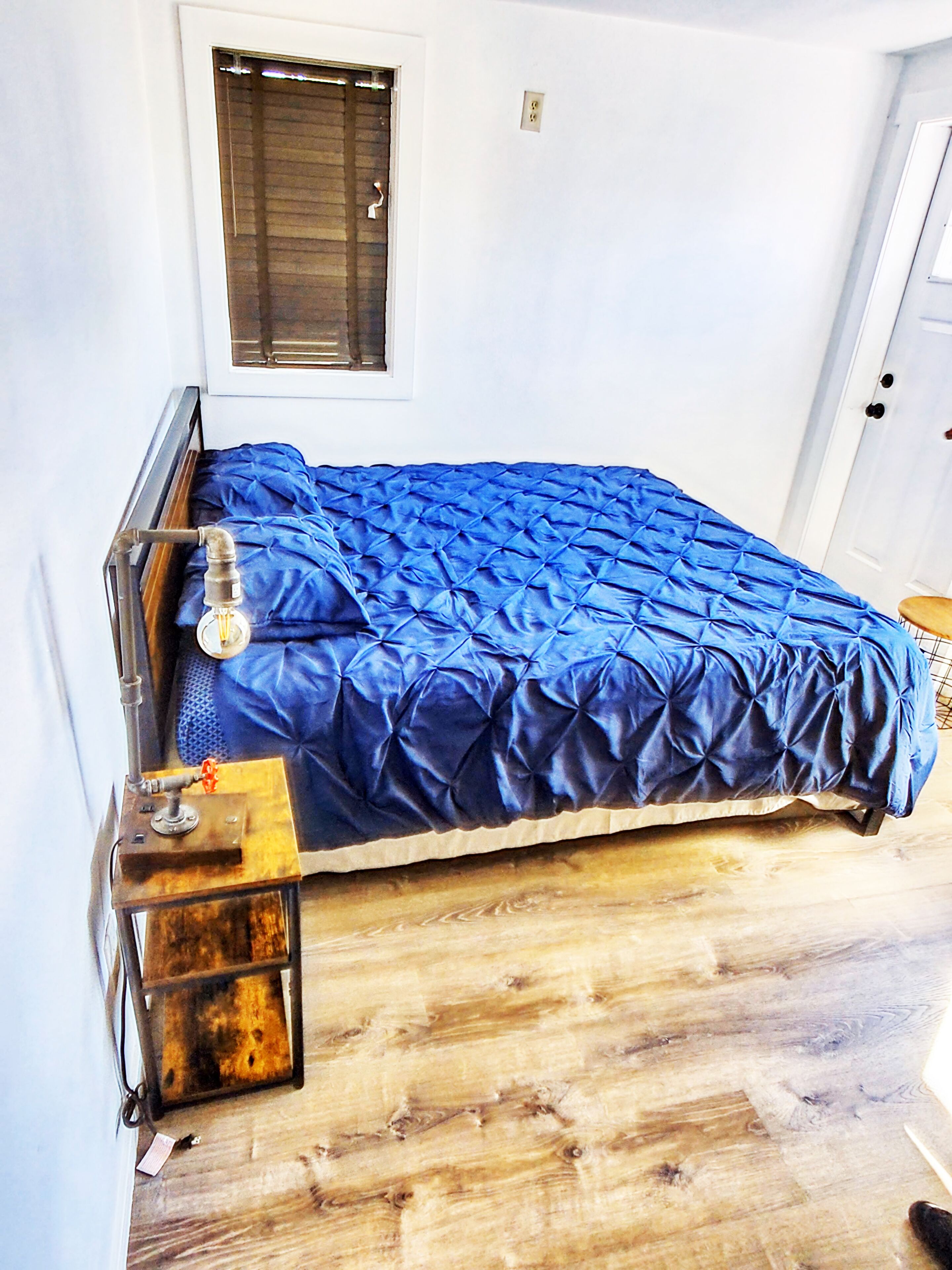 A single bed with a blue cover in a room with white walls and a wooden floor.