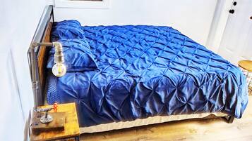 A single bed with a blue cover in a room with white walls and a wooden floor.