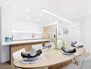 Un espace repas moderne avec une table ronde pour quatre personnes, des chaises blanches et une table en bois clair.