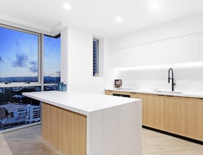 Une cuisine moderne dotée d’un grand îlot central, d’un robinet noir et offrant une vue sur la ville grâce à une grande fenêtre.