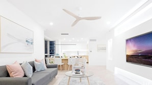 A modern living room with a grey sofa, a glass coffee table, and a large window with a night sky view. - Chevron – 3 Bedroom Superior Unit With Ocean Views (Surfers Paradise)