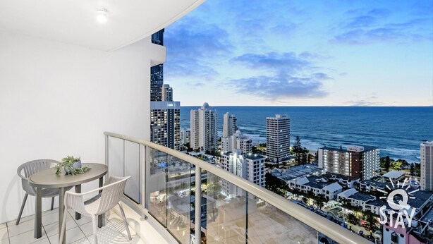 A balcony with a city view overlooking the ocean, featuring a dining area with chairs and a table. - Chevron – 3 Bedroom Superior Unit With Ocean Views (Surfers Paradise)