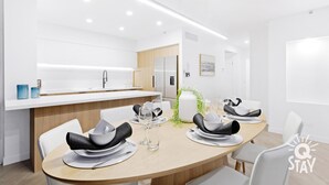 A modern kitchen with white cabinetry, a built-in island, and a dining area with a table set for four. - Chevron – 3 Bedroom Superior Unit With Ocean Views (Surfers Paradise)