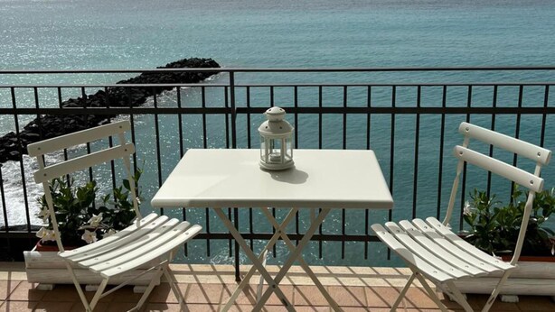 A terrace with a white table and two chairs, overlooking a calm sea and distant hills. - One bedroom apartment with terrace and sea view (Meta)
