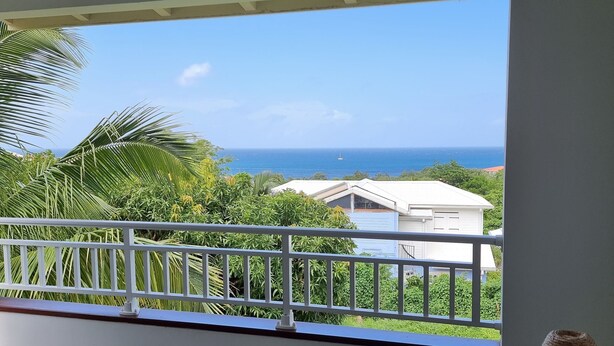 A balcony with a view of the ocean and a white house in the background. - Building (Les Anses-d'Arlet)
