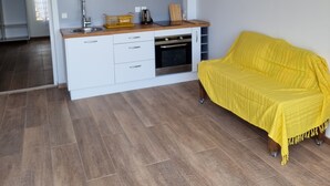A modern kitchen with white cabinets, a built-in oven, and a yellow sofa in a bright living area. - Building (Les Anses-d'Arlet)