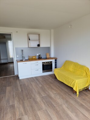 Une cuisine moderne avec des meubles blancs, un four encastré et un canapé jaune dans un salon lumineux.