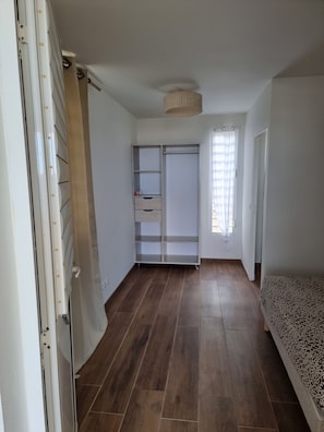 Une pièce avec un plancher en bois, une armoire, un lit et une fenêtre avec des rideaux.